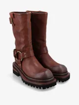 Bota de cuero negro de inspiración biker con caña media. Presenta un diseño robusto con correas ajustables, hebillas metálicas y una argolla decorativa con tachas en el tobillo. Posee suela track de goma para mayor tracción y estabilidad.