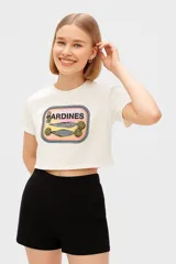 Remera cropped de algodón color crudo con estampado de una lata de sardinas. Tiene cuello redondo y corte holgado.