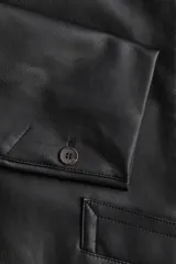 Campera negra de cuero sintético con cuello clásico, cierre frontal con botones, hombreras, bolsillos delanteros con solapa y puños con abertura y botón.