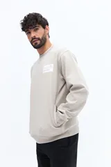 Buzo de algodón color beige claro, con cuello redondo y puños. Presenta un estampado grande en la espalda con texto en gris y blanco, incluyendo referencias a 'London', 'Southbank Art Gallery Centre' y una representación estilizada de la bandera del Reino Unido.