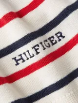 Sweater de punto color crema con rayas horizontales rojas y azul marino. Tiene cuello en V, mangas largas y logo de Tommy Hilfiger bordado en el pecho.