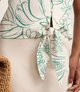 Camisa blanca con estampado floral en tonos verdes, de manga corta, cuello camisero y escote en pico. Tiene cierre con botones y lazo en el bajo.