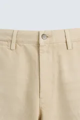 Bermuda de corte amplio color beige, confeccionada en tejido de algodón con efecto lavado. Tiene bolsillos laterales y traseros de parche. Cierre frontal con cremallera y botón.