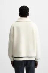 Sudadera color crudo de tejido técnico con cuello alto y cierre de cremallera. Tiene manga larga, corte relaxed fit, bolsillo tipo canguro y rib en puños y bajo con rayas negras.