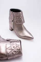 Botas cortas color peltre con taco cuadrado, capellada de cuero y cuello con diseño capitoné y apliques brillantes.
