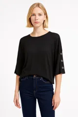 Remera negra de corte holgado y mangas 3/4 con detalle de botones.