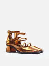 Zapato de tacón cerrado en tono dorado, con parte delantera cerrada y tiras en el empeine y tobillo.