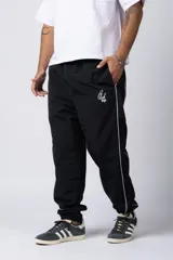 Pantalón de jogging negro de taslan con corte holgado, cintura elástica con cordón ajustable, bolsillos laterales y puños elásticos. Presenta una franja blanca a lo largo de la pierna y logo bordado en blanco.