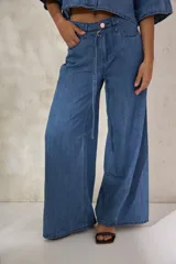 Pantalón de denim azul medio, tiro medio, de corte ancho (wide leg) con caída fluida. Presenta una presilla metálica decorativa en la cintura.