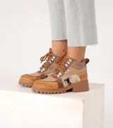 Borcego de cuero color marrón con paneles de tela texturizada y estampado animal print. Tiene cordones marrones, herrajes metálicos y suela de goma con plataforma.