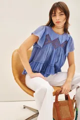 Camisa azul de algodón liviano con cuello redondo y gota en la espalda. Presenta detalle de bordado calado, terminación de volado en mangas y ruedo.