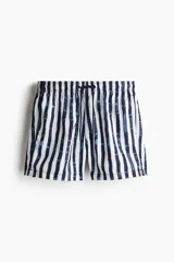 Short de baño blanco con rayas verticales azules, cintura elástica con cordón ajustable, bolsillos laterales y bolsillo trasero con cierre autoadherente. Cuenta con suspensor interior de malla suave.