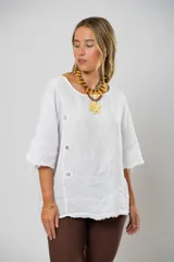 Blusa blanca de lino con corte asimétrico, mangas 3/4 con botones y cuello redondo amplio.