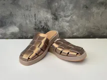 Sueco de cuero color oro con diseño tejido y suela de goma color beige.