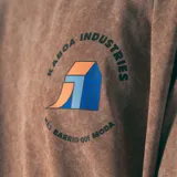 Remera oversize color beige con efecto gastado, cuello redondo y estampado pequeño en el pecho con el logo de la marca Kaboa Industries y la frase 'Más barrio que moda'.