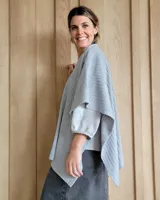 Ruana tejida en lana color gris claro, de corte amplio y diseño abierto.