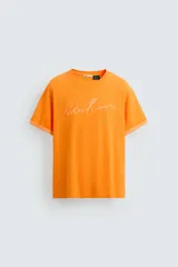Camiseta naranja de algodón con cuello redondo y manga corta con vuelta. Estampado frontal con la firma del artista Otis Kwame Kye Quaicoe.