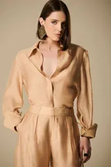 Camisa color beige de organza con acabado satinado, cuello clásico y mangas largas con puños abotonados.