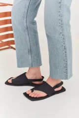 Sandalias de cuero color crema con tira ancha sobre los dedos, suela plana cuadrada color negro y tira trasera ajustable.