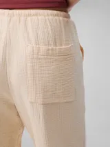 Pantalón de corte recto color beige, de gasa doble con textura arrugada, cintura elástica con cordón ajustable, bolsillos laterales y trasero.