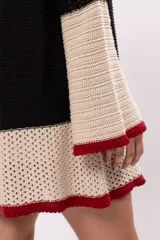 Minivestido tejido a crochet con rayas horizontales en color crudo y negro, con mangas acampanadas y terminaciones en color bordó.