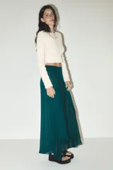 Falda midi verde esmeralda de satén, de tiro alto y corte evasé, con bajo asimétrico y forro interior.