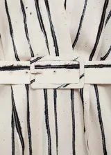 Mono largo de tejido satinado color crudo con rayas verticales negras. Tiene escote cruzado en V, sin mangas, cinturón desmontable con hebilla cuadrada y cierre trasero invisible.