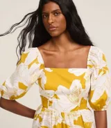 Vestido midi de tricolina con estampado floral en tonos amarillo y blanco. Tiene escote cuadrado, mangas abullonadas cortas, lastex en la espalda y recorte fruncido en la cintura.