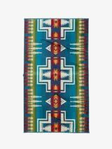 Toalla extragrande de felpa suave, con un lado de acabado aterciopelado y un diseño de bucles que garantiza una absorción superior. Presenta un diseño geométrico con patrones tribales en tonos azules, verdes, rojos, amarillos y blancos.