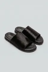 Sandalias planas negras tipo slide, con capellada ancha de pelo corto. Tienen suela de caucho expandido y base plana de 3 cm de altura.