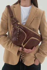 Riñonera marrón de cuero con textura croco, doble bolsillo frontal con cierres dorados y correa ancha regulable con patchwork de cueros lisos y grabados.