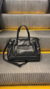 Cartera negra de simil cuero con correa corta y correa larga ajustable. Tiene cierre principal, bolsillos interiores y exteriores en la parte delantera y trasera.