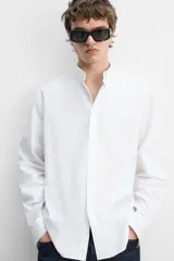 Camisa blanca de corte regular fit confeccionada en popelín de algodón. Tiene cuello abotonado, manga larga con puños abotonados y cierre frontal con botones.