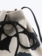 Bolso bandolera tipo bucket con estampado de flores en blanco y negro, con ajuste superior de cordón y correa larga de hombro negra.
