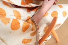 Capa de lana color crudo con estampado de hojas de eucalipto en tonos naranja y marrón. Tiene cierre con broches a presión en el escote y ojales metálicos con cintas para anudar en los laterales.