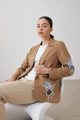 Blazer color tostado con bordados florales en azul y negro en la solapa y en la manga.