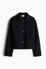 Campera corta negra de sarga de algodón, corte holgado, con cuello clásico, cierre frontal con botones marrones, mangas largas y bolsillos de parche delanteros.
