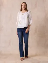 Blusa blanca de gasa con bordados florales, corte holgado, mangas 3/4 acampanadas con detalle de puntilla y forro interno.