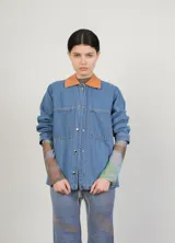 Campera de jean con cuello clásico, cierre frontal con botones metálicos, dos bolsillos de parche en el pecho y estampado floral en tonos verdes y marrones.