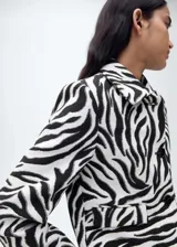Chaqueta con estampado de cebra, cuello de solapa, diseño recto, cierre delantero con botones, forro interior y dos bolsillos de solapa en la parte frontal.