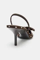 Zapato de tacón con estampado de lunares blancos sobre fondo marrón. Presenta un lazo decorativo en la parte delantera, tira trasera con elástico y punta fina. La altura del tacón es de 6 cm.