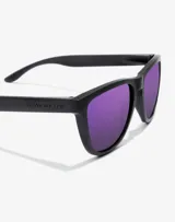 Lentes de sol Hawkers unisex, modelo One Raw, con montura cuadrada negra y lentes polarizadas color violeta.