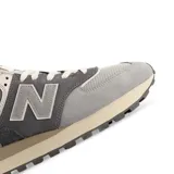 Championes New Balance 574 de caña baja, con capellada de gamuza gris, puntera de malla gris claro y logo "N" en cuero gris.