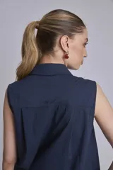 Camisa azul marino sin mangas con cuello clásico, abotonada al frente y detalle de plisados verticales en el pecho.
