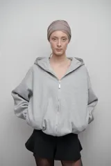 Campera gris confeccionada en felpa de algodón extra suave, con cierre metálico, bolsillos laterales y amplia capucha. Silueta oversize unisex.
