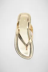 Sandalia plana dorada de cuero, con tira delantera para el dedo y suela delgada.