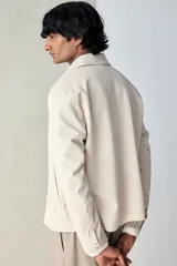 Campera color beige de tejido suave con cuello, cierre frontal, puños ajustables con botón a presión y bolsillos insertados al bies. Corte estándar y mangas forradas.