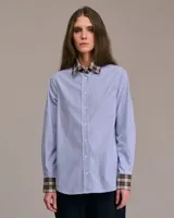 Camisa celeste a rayas verticales blancas, de corte recto, manga larga y cuello clásico con interior a cuadros.