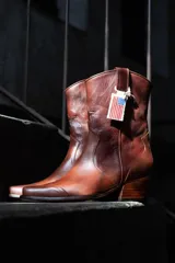 Bota texana de cuero color marrón con detalles de costuras y diseño tradicional. Tiene caña media, puntera marcada y taco bajo.