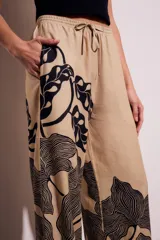 Pantalón de lino color beige con estampado de hojas negras, corte flare y tiro alto.